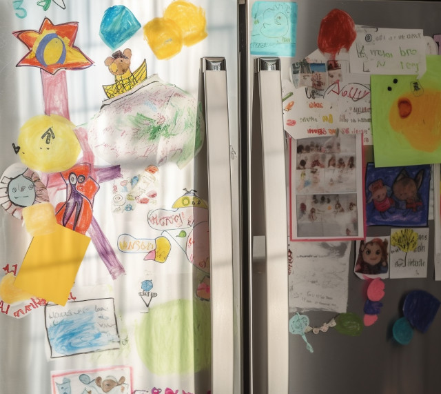 colorful children's drawings in crayon, covering a fridge